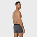 Man in dark gray NEW TENA Men Protective Boxers, glancing back, showcasing sleek design and fit with a silver chain against a light gray background.