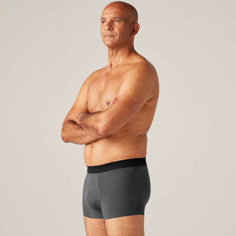 TENA Men Protective Boxers Light: A man stands confidently wearing grey incontinence boxer shorts, showcasing a comfortable, discreet fit with built-in protection.
