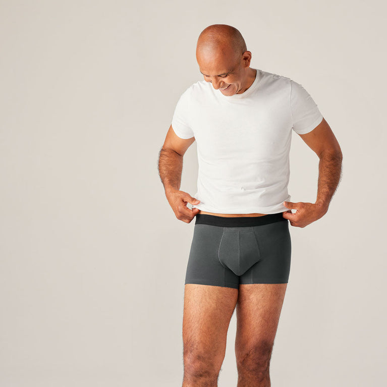 TENA Men Protective Boxers Light: A man wears a white shirt and grey boxer briefs, showcasing washable, discreet incontinence protection with a comfortable fit.
