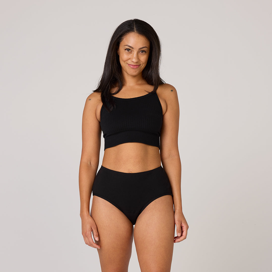 Woman wearing TENA Organic Cotton Underwear, black ribbed crop top and high-waist briefs, showcasing comfort and fit for light bladder leaks.