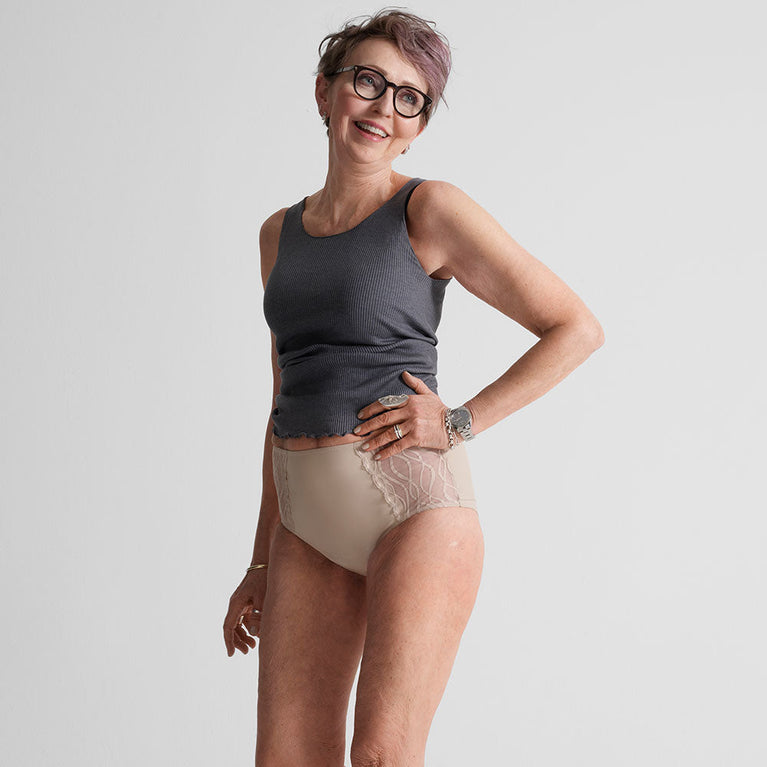 Woman smiling, wearing Silhouette Classic Washable Underwear for Light Incontinence, featuring a grey tank top and beige underwear, offering discreet, breathable protection and comfort.