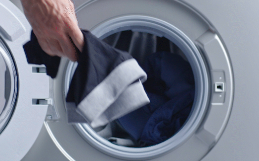 Male hand placing a black men's washable incontinence boxers with a grey waistband inside a front-loading washer.