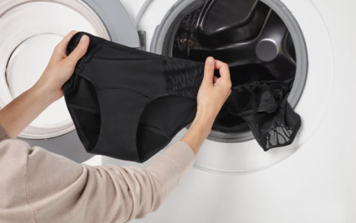 Hands place a pair of black Silhouette Hipster washable incontinence underwear into a front-loading washing machine in a laundry setting.